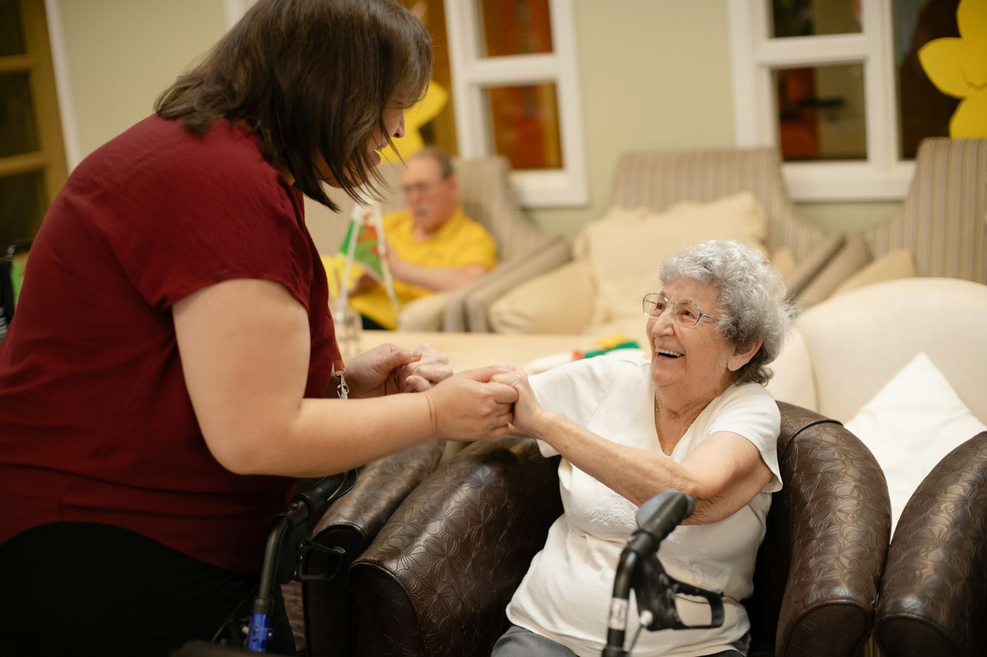 A caregiver smiling and holding hands with an elderly woman in her home